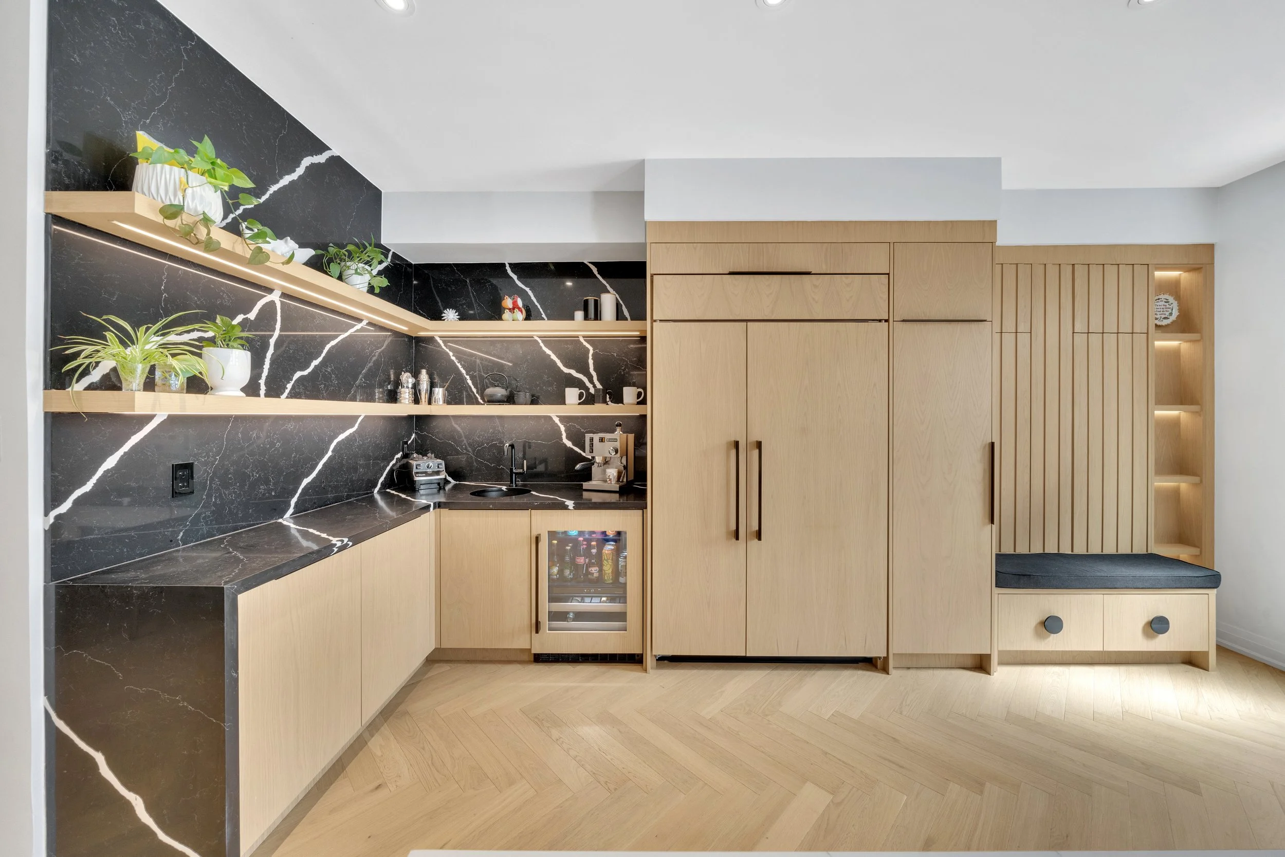 Modern kitchen with black marble countertops, light wood cabinets, open shelving, and built-in wine cooler.