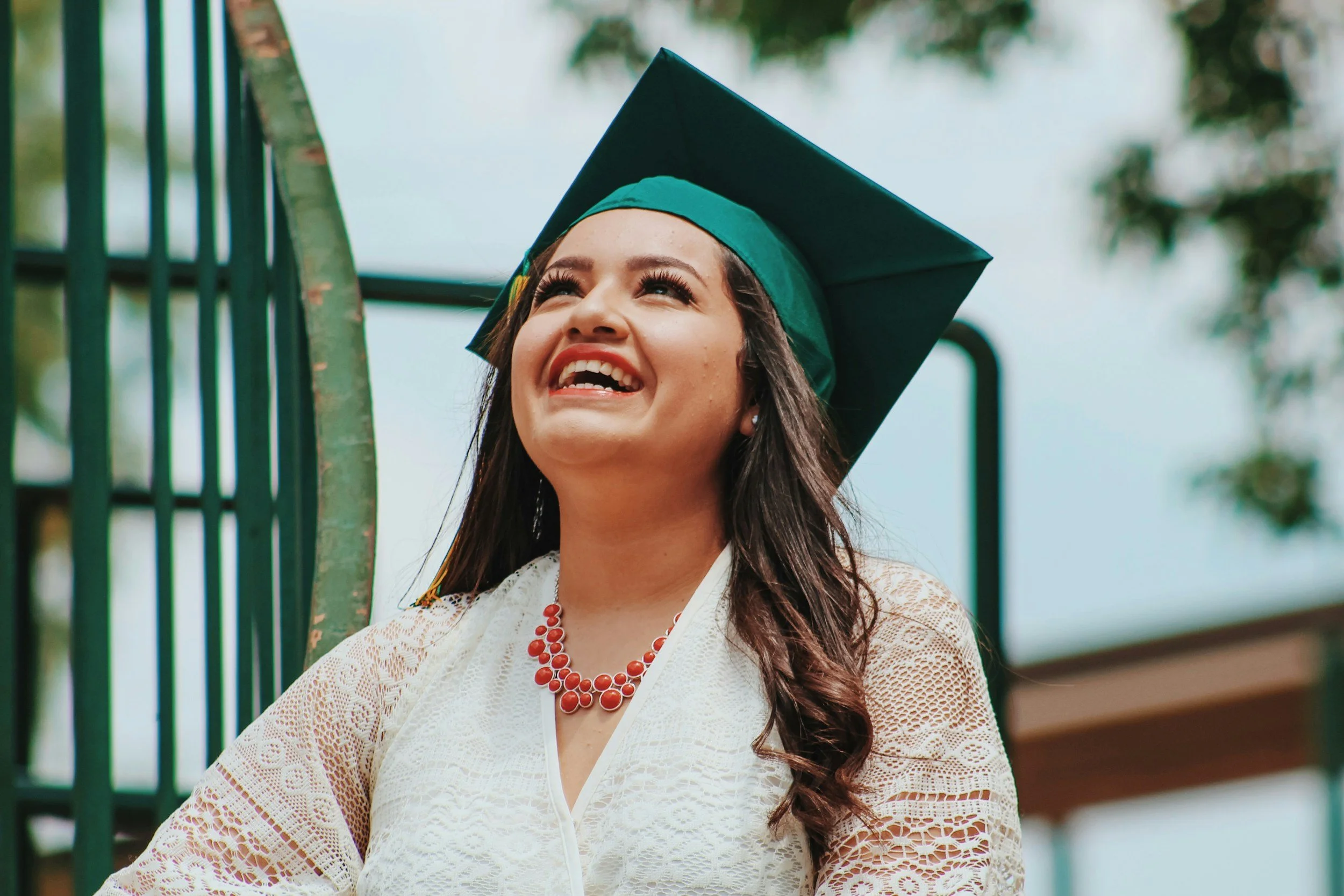 A young woman wearing a green graduation cap and a big smile. One can assume the smile is becuase she got into a great school thanks to True Honors College Consulting.