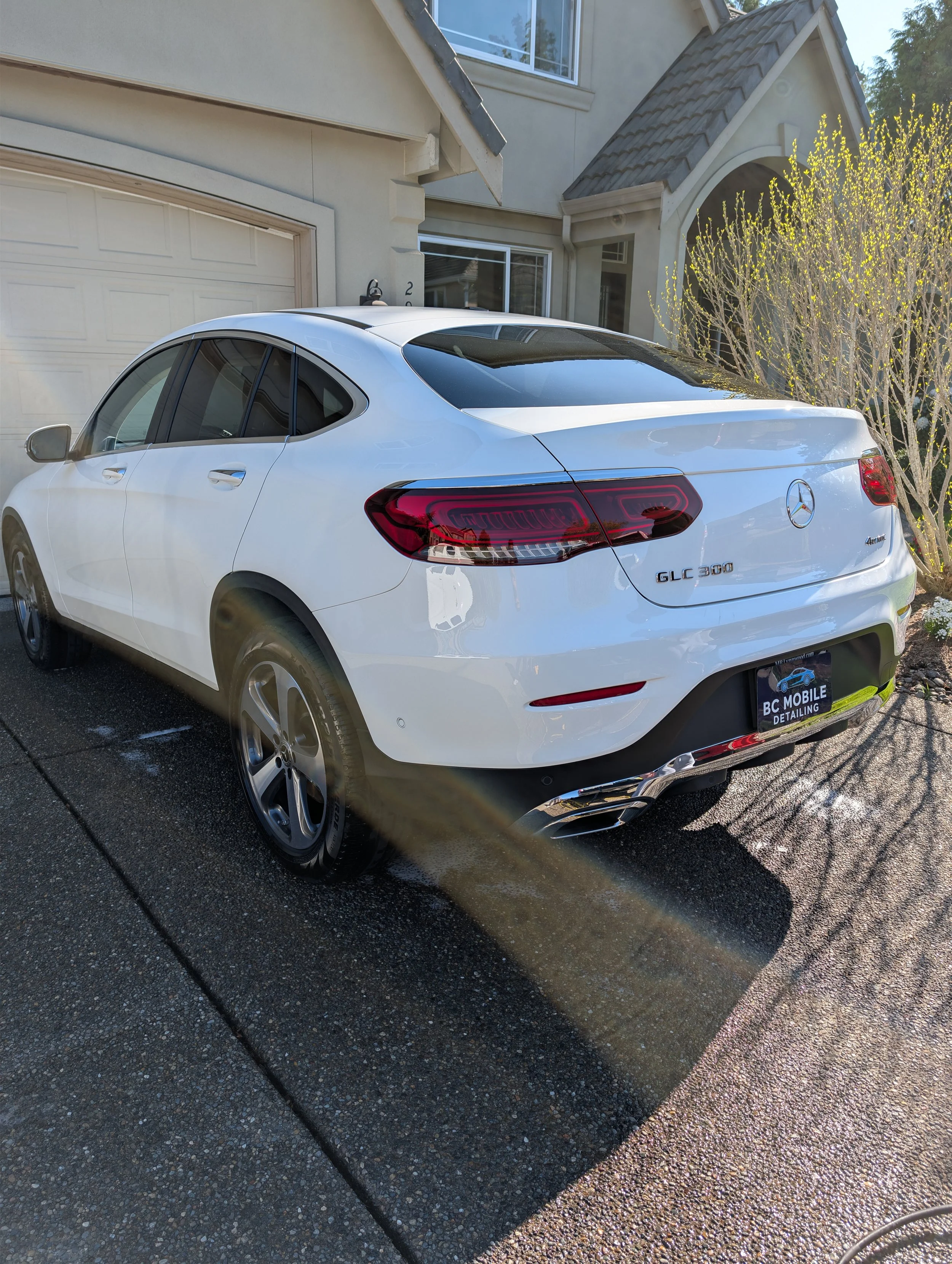 A white Mercedes-Benz GLC 300 parked in front of a house on a sunny day with a shadow cast on the pavement.