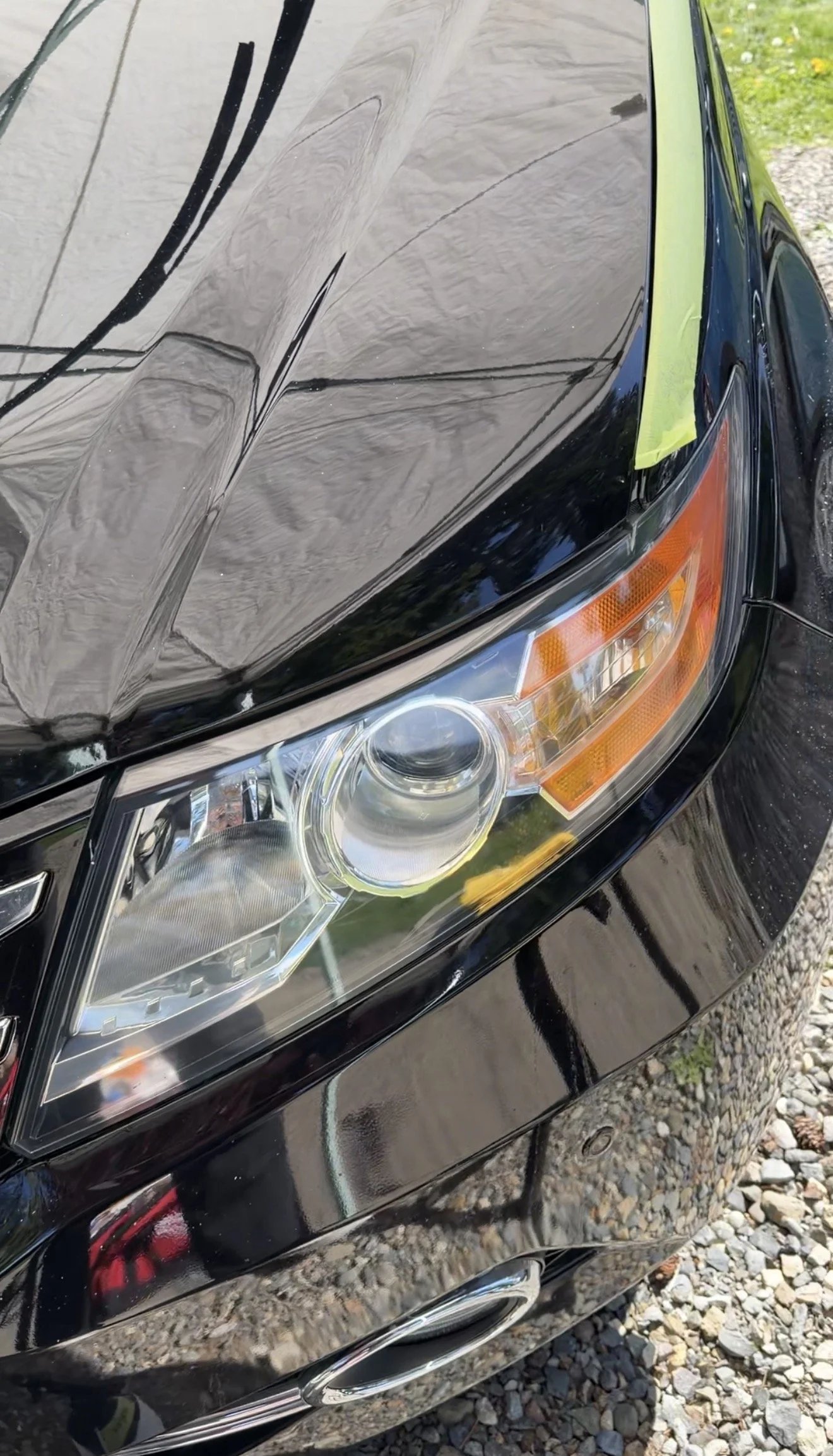 Close-up of a black car's front right corner, showing the restored headlight, that is no longer yellow and damaged, Showing the headlight restoration.