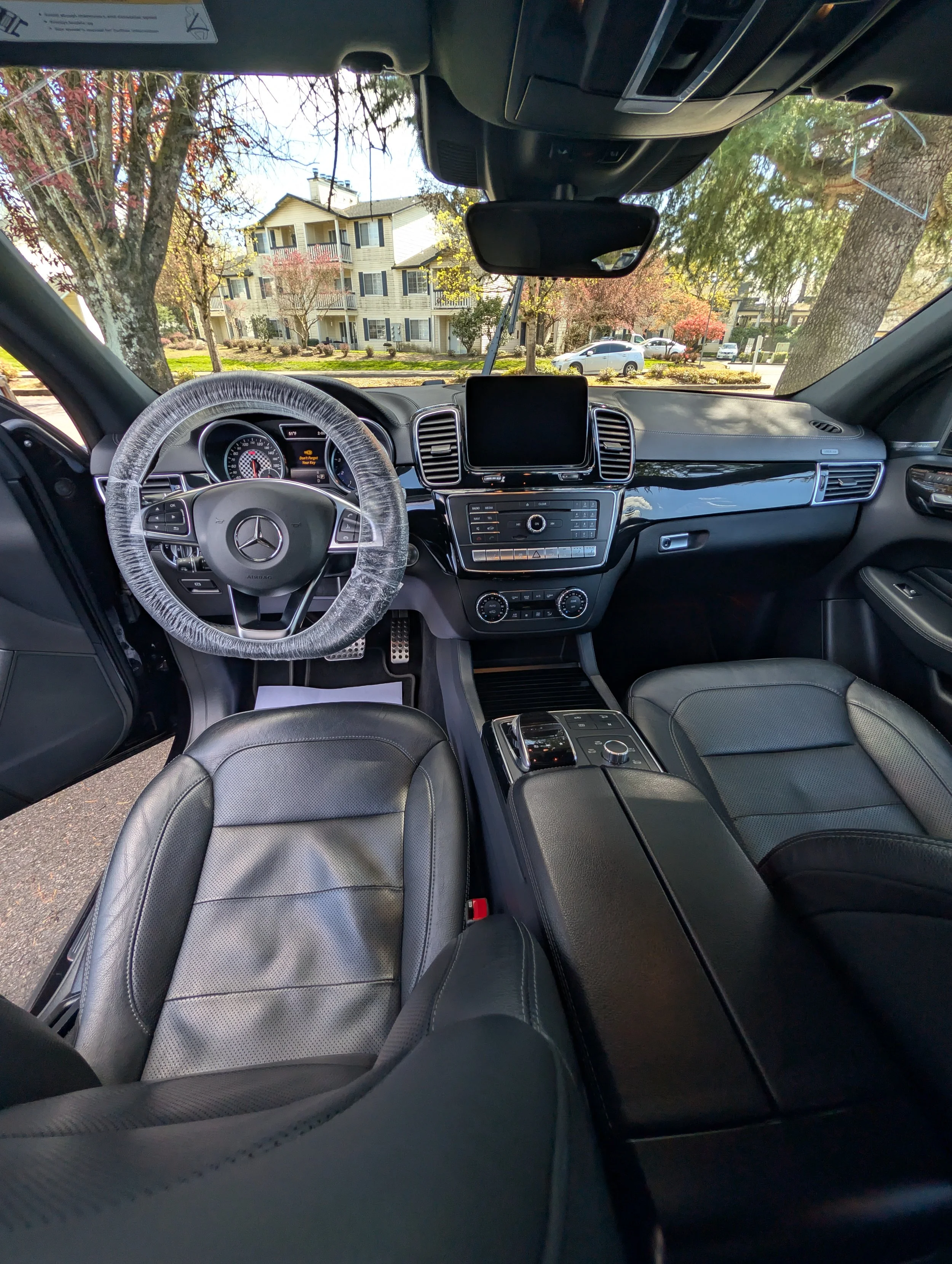 View of the interior of a Mercedes-Benz car showing the dashboard, steering wheel wrapped in plastic, and black leather seats. The perfect express detailing package.