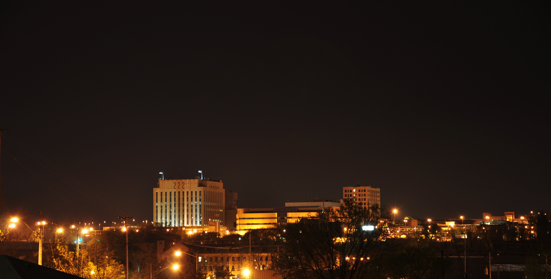 Nighttime cityscape with illuminated buildings and streetlights under a clear dark sky.