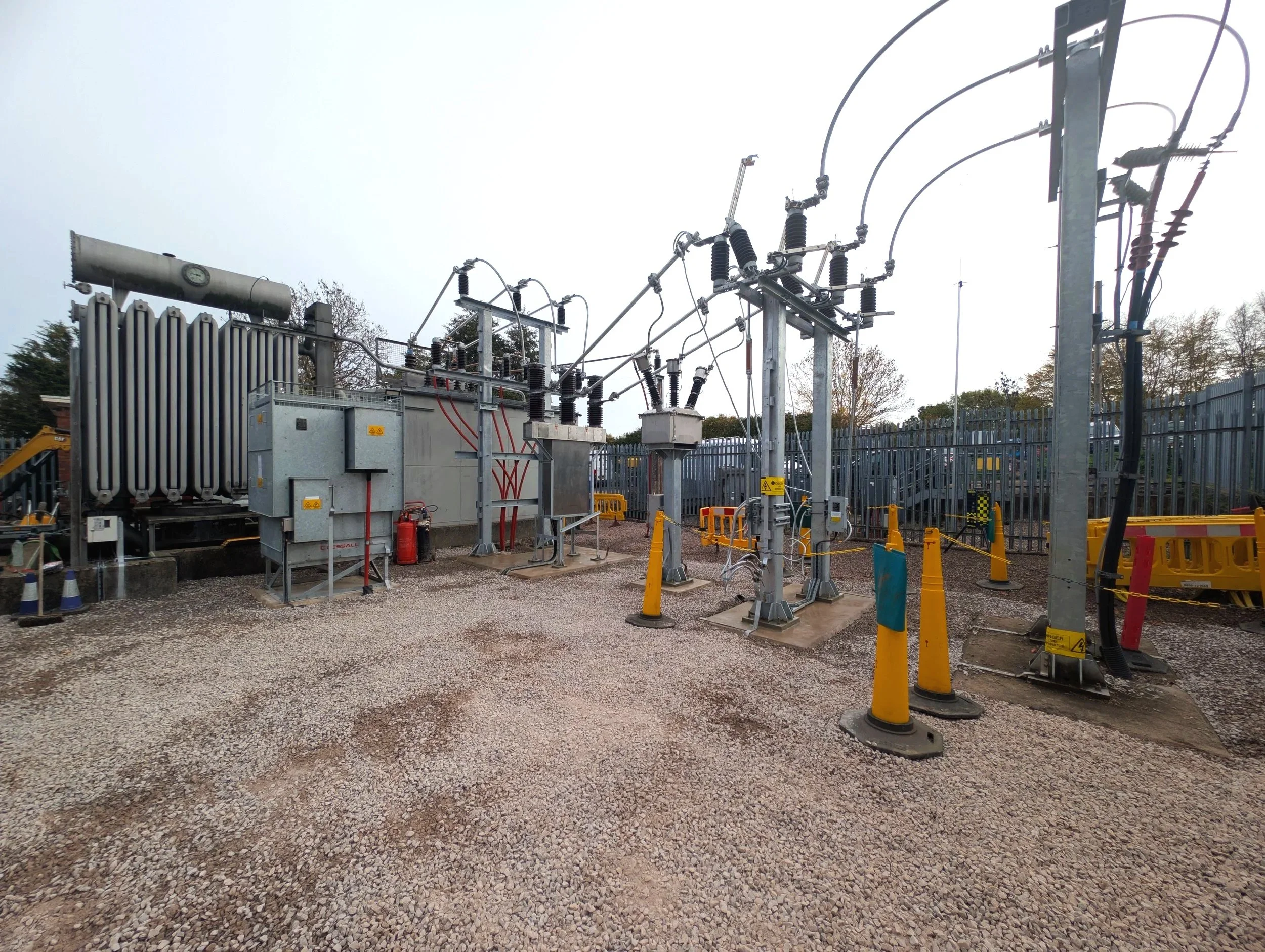 Electrical substation with transformers, insulators, and wiring surrounded by yellow safety cones and fencing