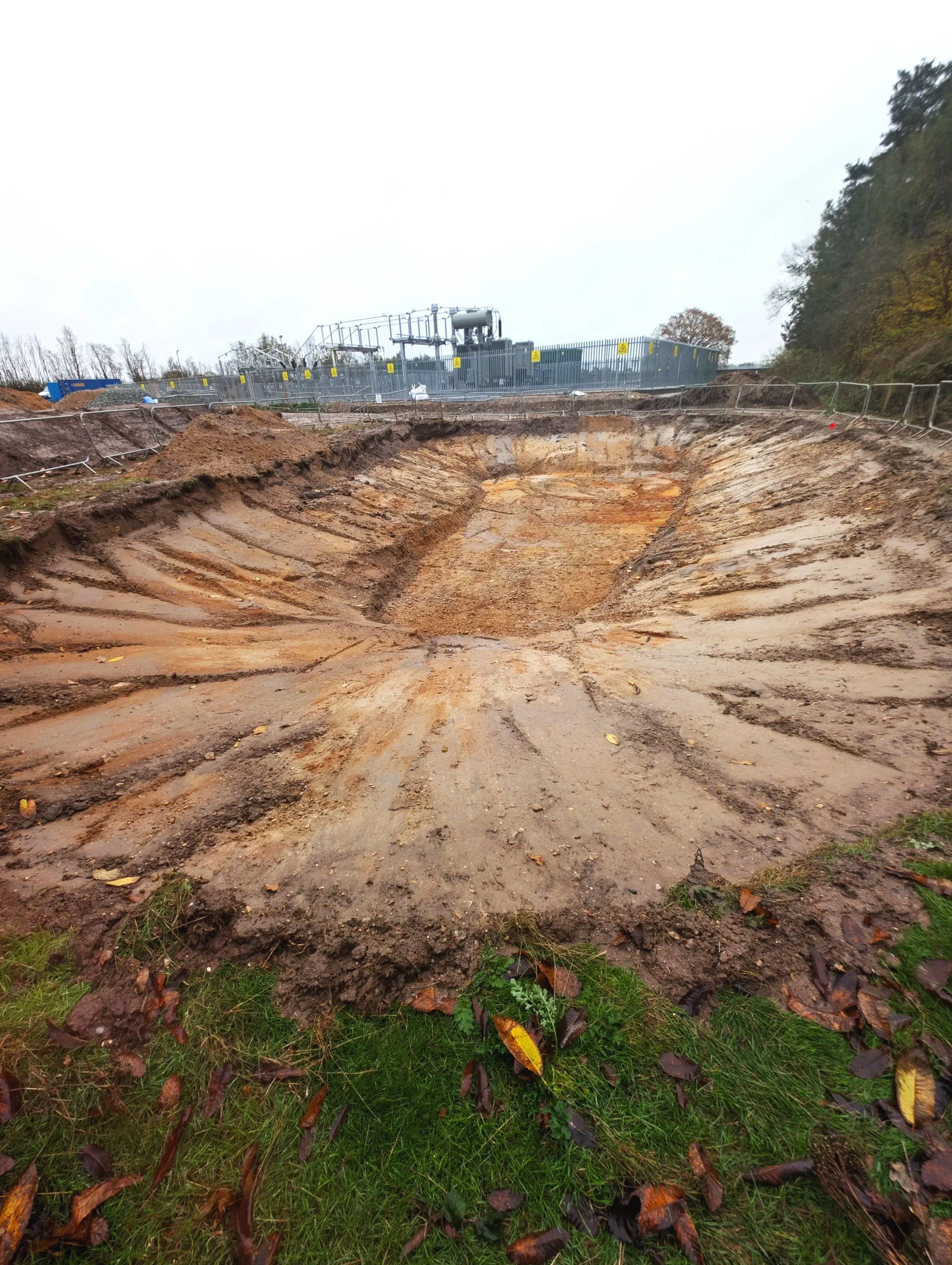 Deep excavation site, with metal safety barriers and industrial equipment in the background.