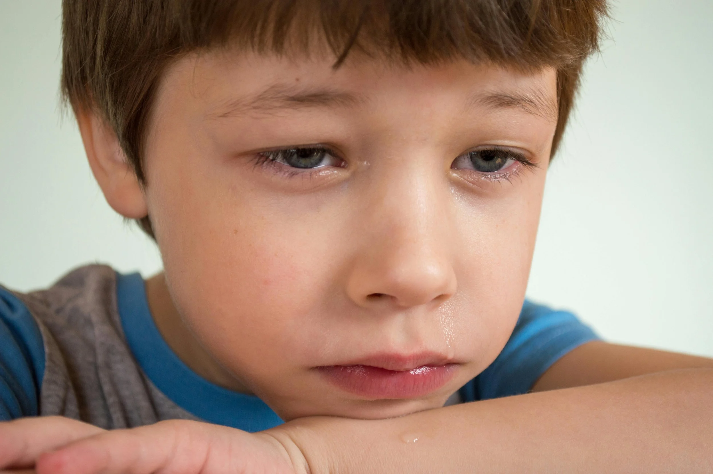 Child sitting alone and worried at school while parents learn how to notice teasing, hesitation, and school dread early