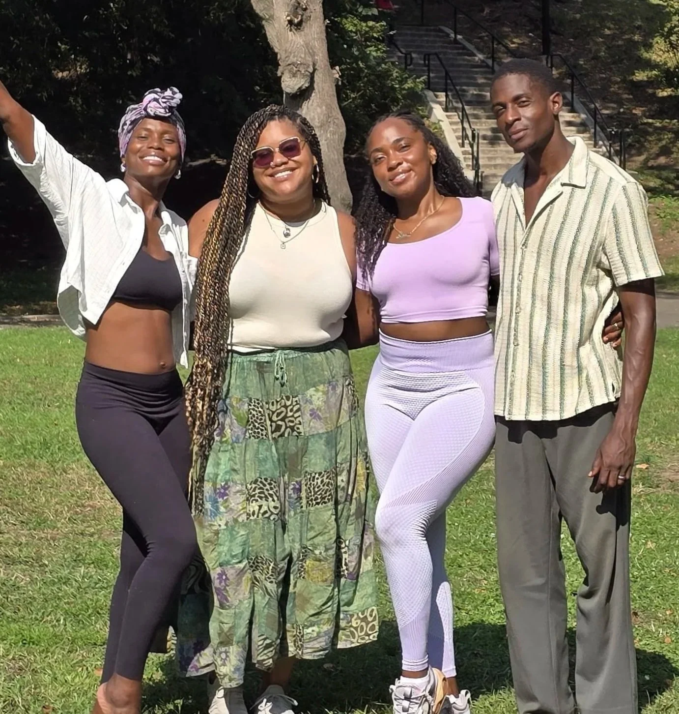 four people pose in a park with trees and stairs in the background