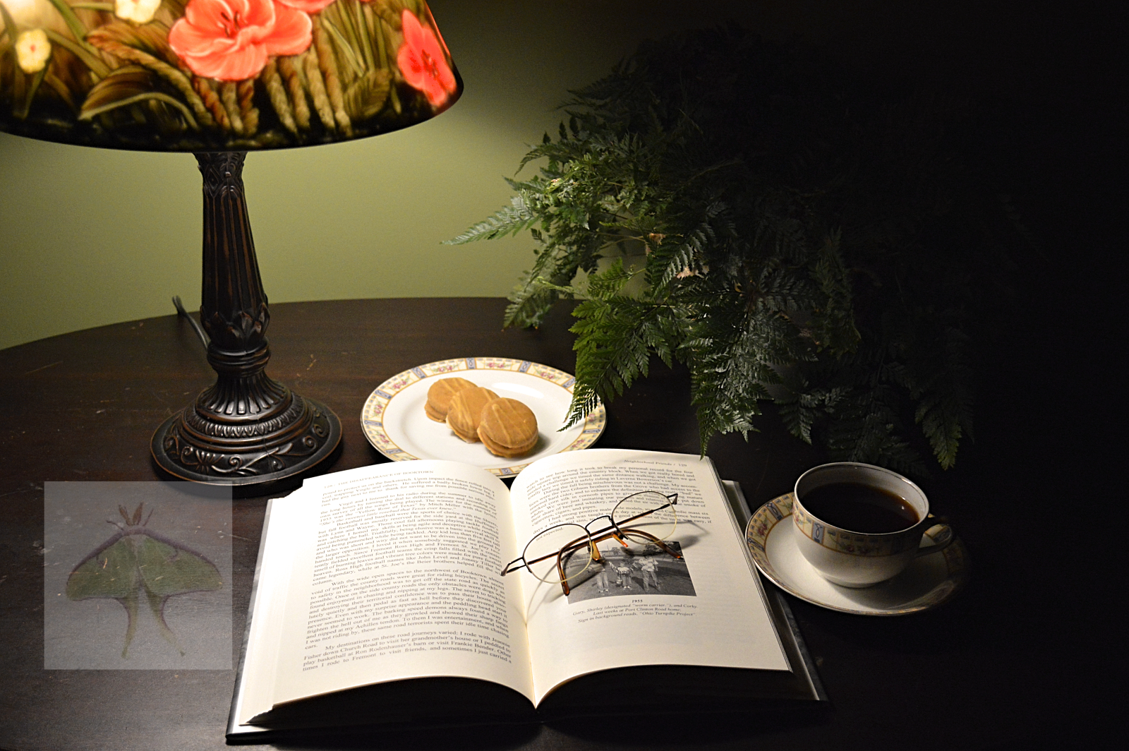 A Cup of Tea and a Good Book- To evoke a moody and authentic atmosphere, I designed a quiet reading nook in the den.  The composition features an antique table paired with a softly lit, reverse-painted lamp, a delicate plant, a small snack, and a ste