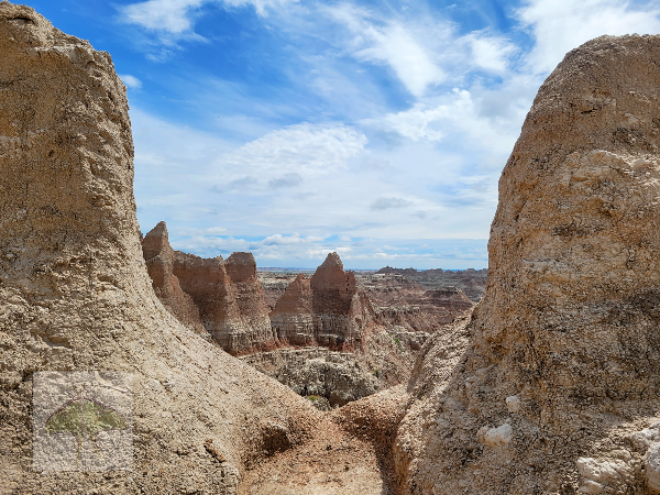 Framed-Peering through two rugged pinnacles, this panoramic canyon view unfolds. Deep shadowy crevasses carve through resilient rock, revealing striking bands of rust red and pale yellow. This seemingly endless Badlands wilderness stretches into the 