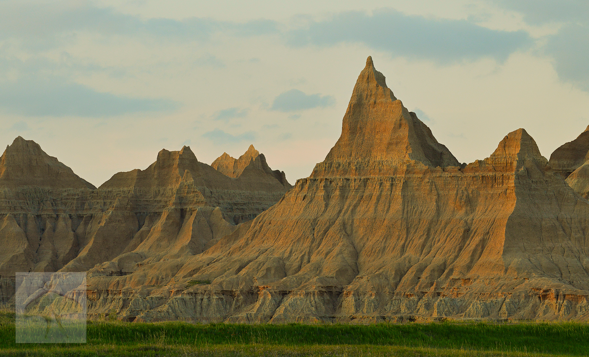 Dusk in the Badlands- The sun kissed the high peaked ridge of the Badlands before completely slipping away. Swaying in the evening breeze, dark green grass created a soft contrast against the harshness of the severely sculpted ridge. As the fading su