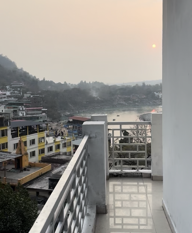 View from a balcony overlooking a river at sunset, with residential buildings on the left and hills in the background.