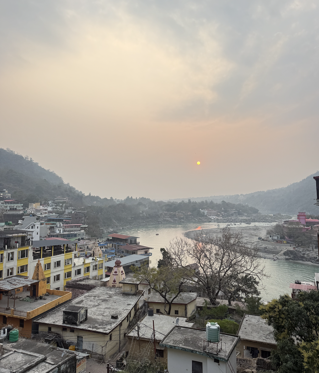 Sunset over a river valley with hills, residential buildings, and trees in a mountainous area.