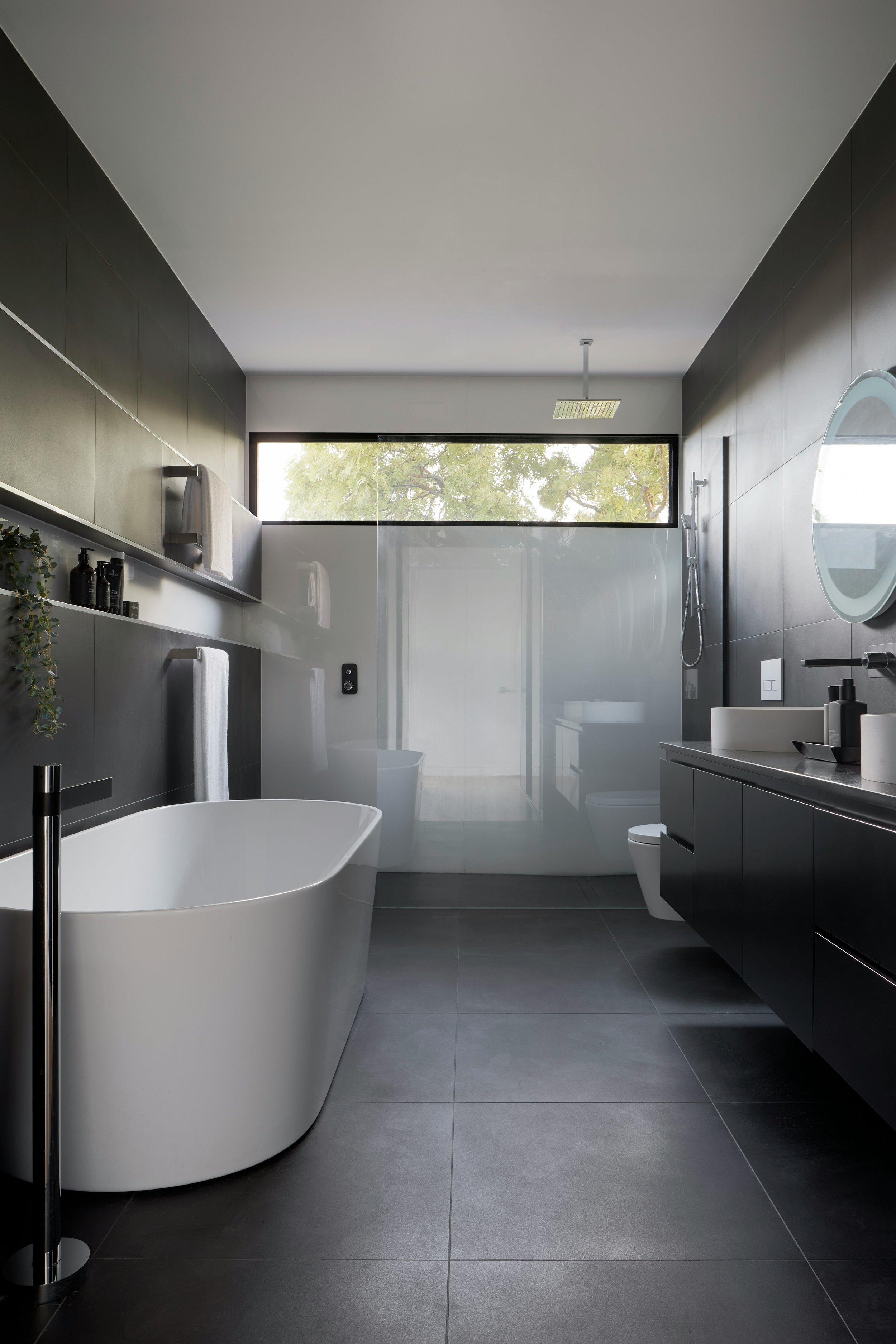 Modern bathroom with freestanding tub, glass shower, dark tiles, and large mirror.