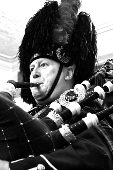 A man dressed in traditional Scottish bagpiper attire, including a feathered hat, playing bagpipes.