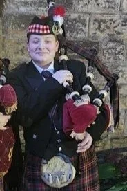 Person dressed in Scottish traditional attire playing bagpipes outdoors