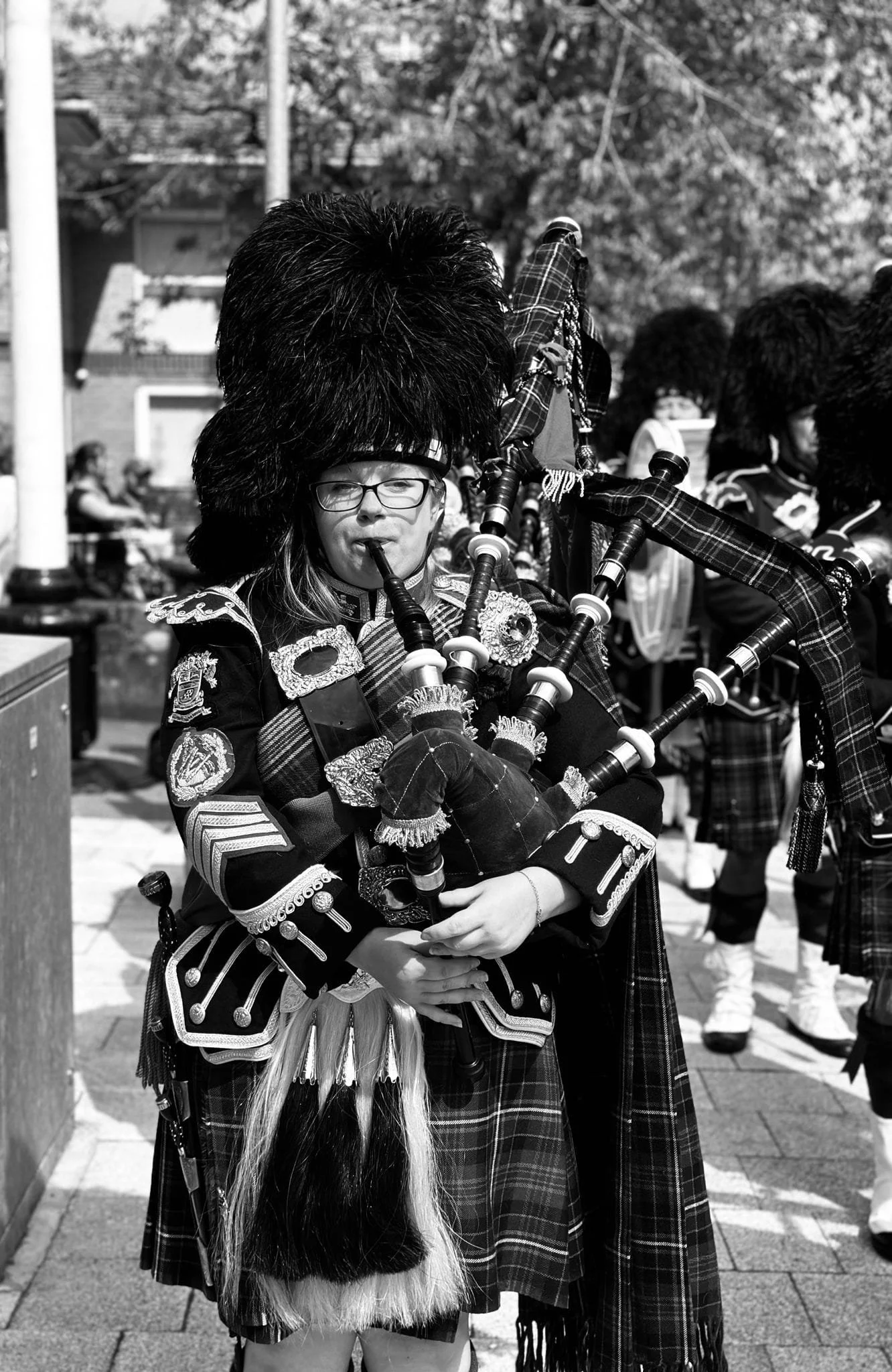 A person wearing traditional Scottish attire, including a kilt, playing the bagpipes outdoors during a parade or event.