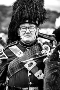 A person dressed in traditional Scottish Highland dress, playing bagpipes outdoors.