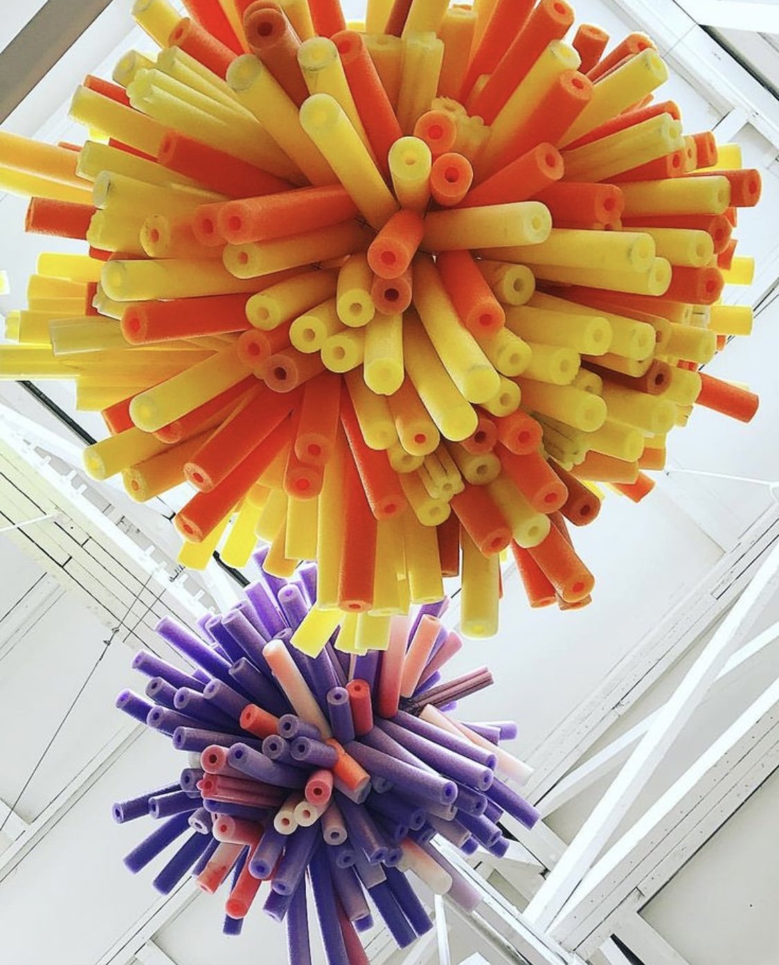 Ceiling decoration with large colorful spheres made from foam pool noodles in yellow, orange, purple, and pink.