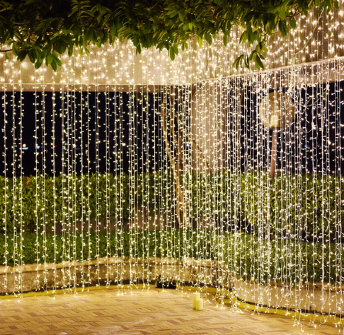 Outdoor scene with cascading string lights amid greenery and a nighttime setting
