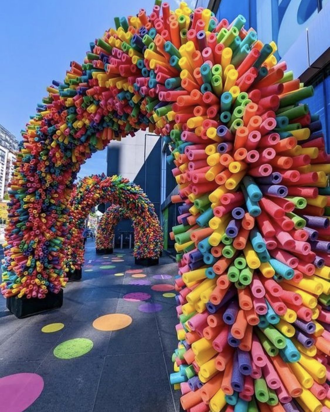 Colorful arches made of pool noodles in an outdoor urban setting with polka dot decorations on the ground.