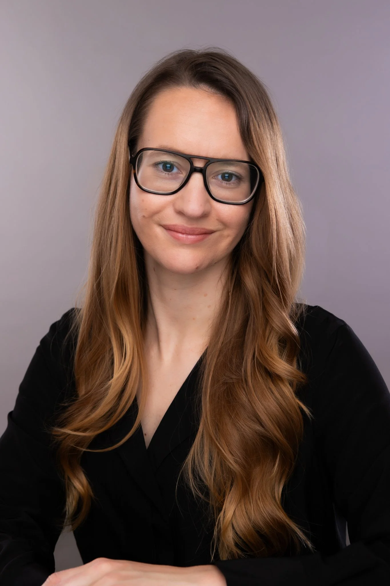 Black and white portrait of a woman with glasses and long hair, smiling and wearing a dark top.