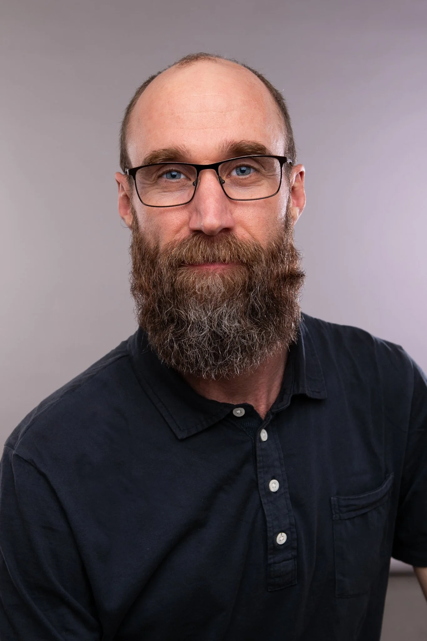 Black and white portrait of a man with a beard and glasses wearing a collared shirt.