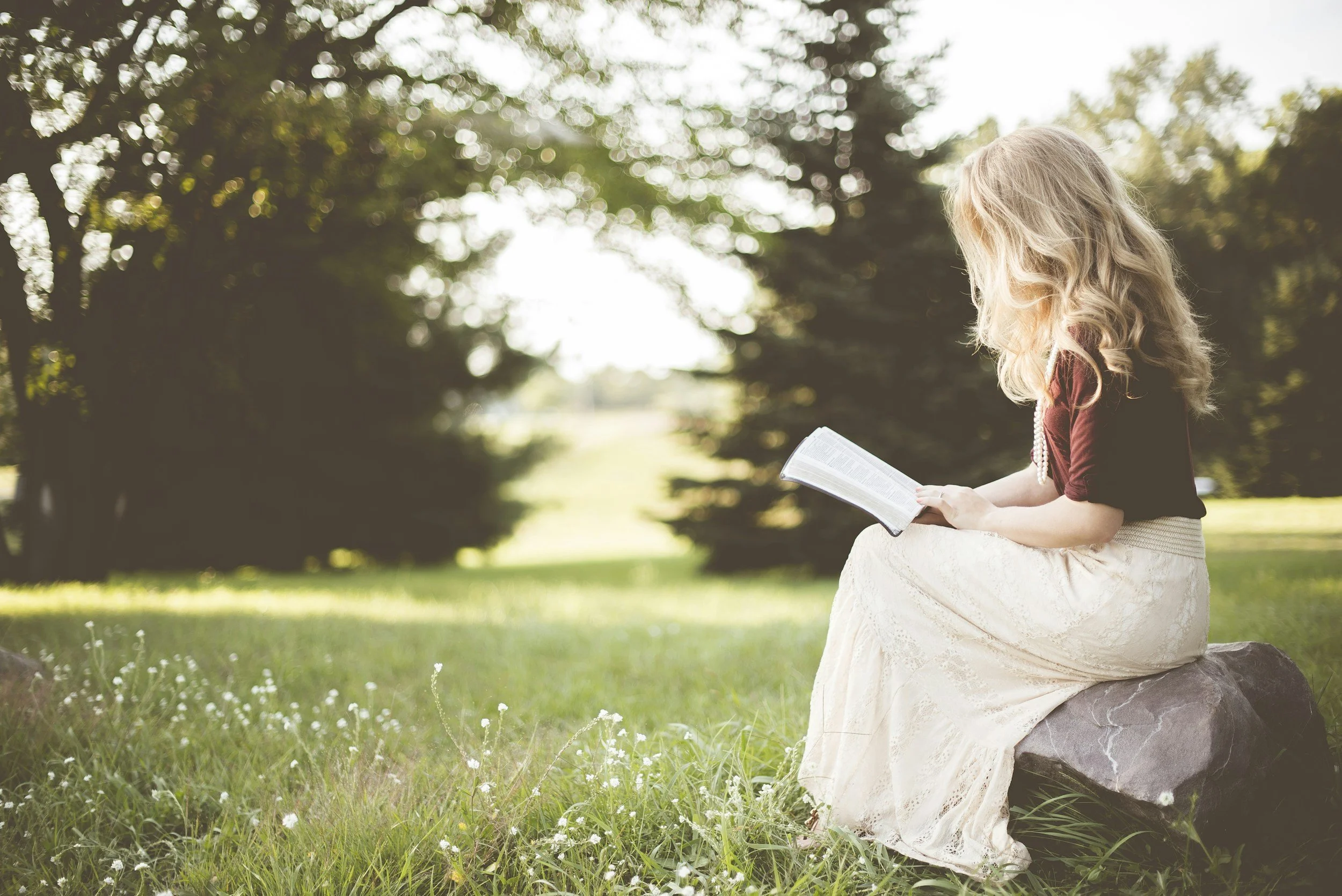 blonde girl sitting in nature reading from the Bible, Christian girl aesthetic