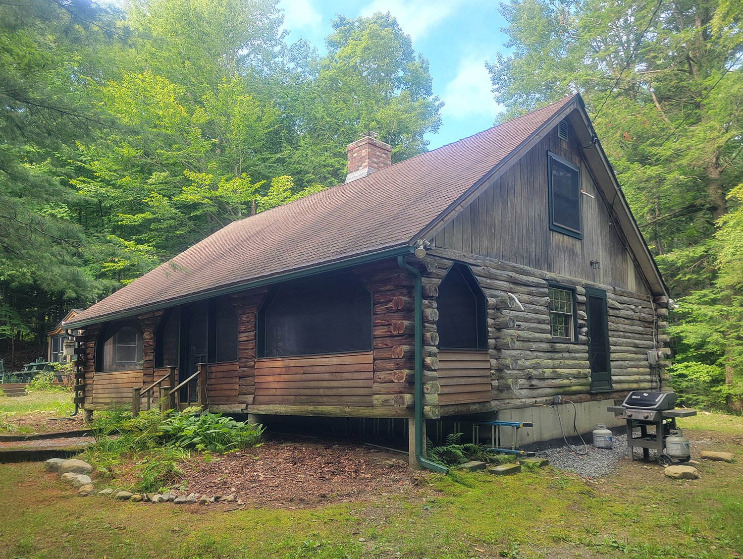 Before, showing the greyed logs and flat siding at the gable ends and sections of the porch.