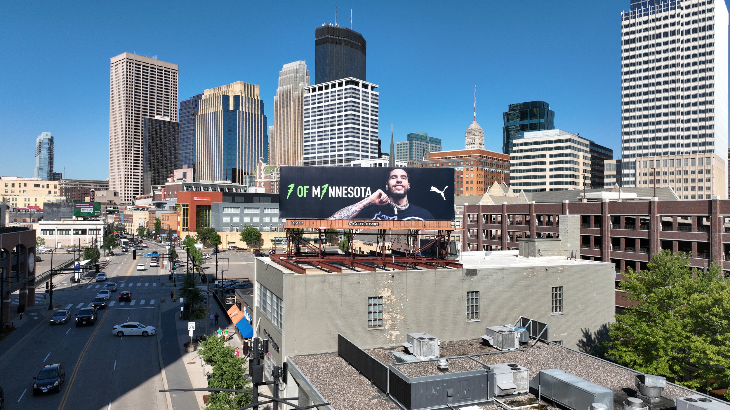 City skyline with tall skyscrapers, a billboard of LaMelo Ball, and busy city streets below under a clear blue sky.