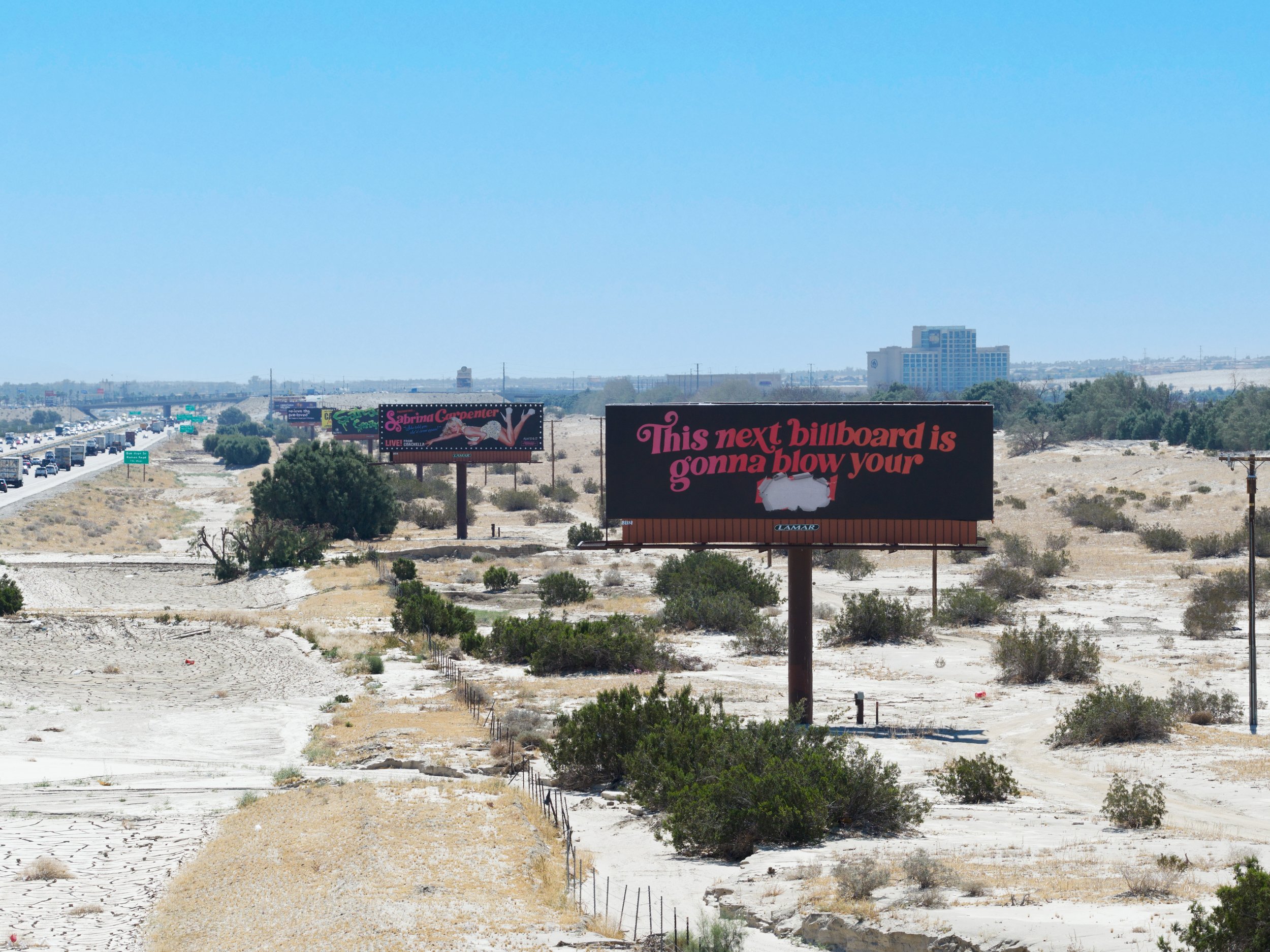 Billboard advertisements along a desert highway, with one promoting a live performance by Sabrina Carpenter and another with partially visible text about a billboard.