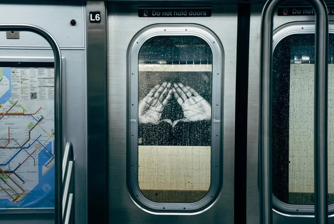 Rainy subway door with a painted hand symbol forming a heart shape, with a subway map partially visible on the left.
