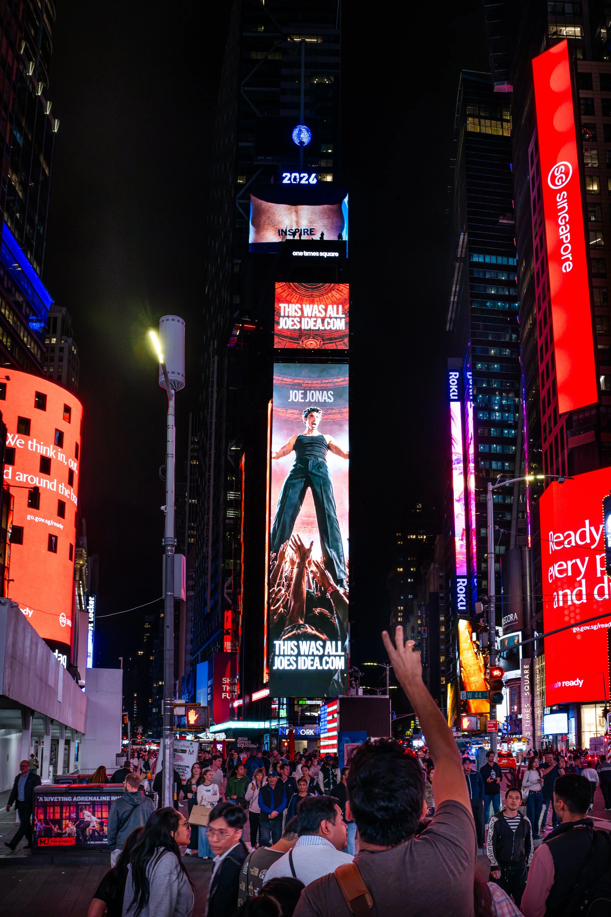 Crowd of people in Times Square at night with bright digital billboards displaying advertisements and messages.