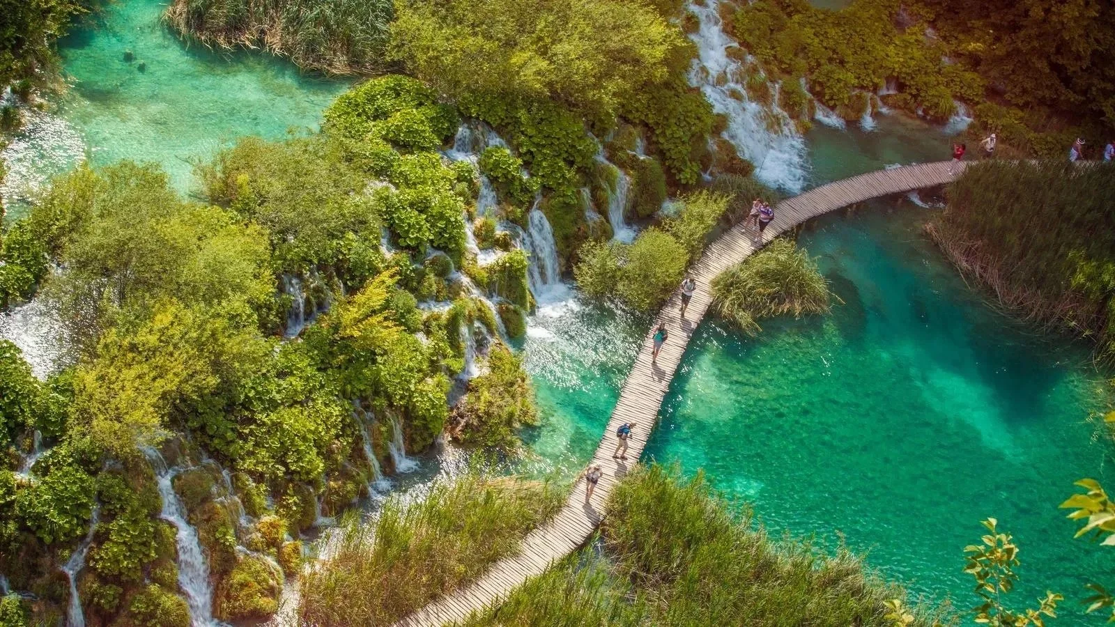 Aerial view of a wooden boardwalk winding through turquoise lakes and lush greenery with small waterfalls, in Plitvice Lakes National Park, Croatia,.