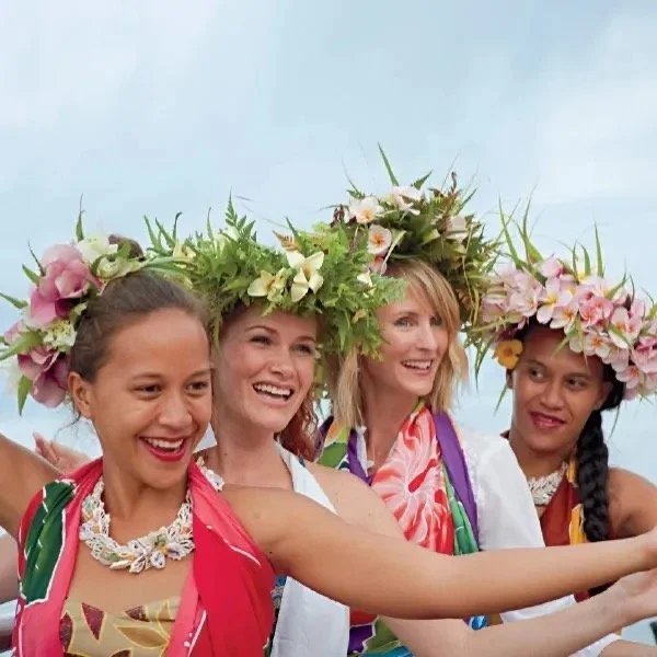Four women wearing flower crowns and traditional clothing, smiling.