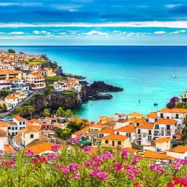 Scenic coastal town with colorful buildings, red tile roofs, cliffs, and vibrant blue ocean.