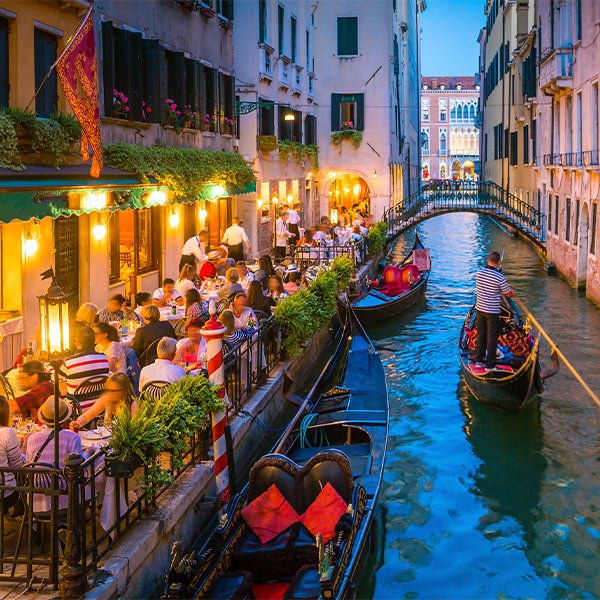 A scenic view of the Cliffs of Moher in Ireland, showing dramatic, steep cliffs rising above the Atlantic Ocean with lush green grass on top and sunlight illuminating the rugged rock faces. The sea below is calm with gentle waves.