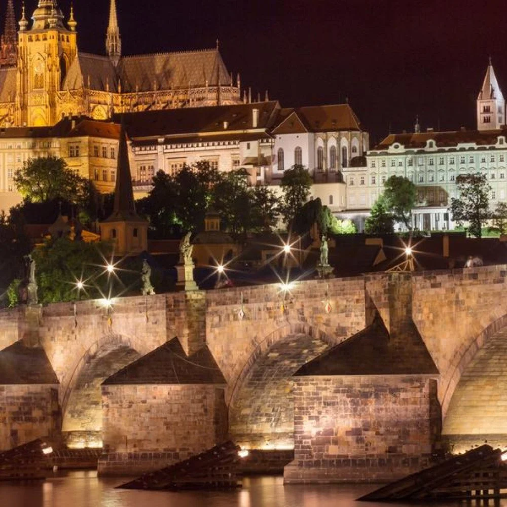 Group of tourists walking on a cobblestone street with a tour guide holding a sign, surrounded by historic stone buildings under a blue sky with clouds.