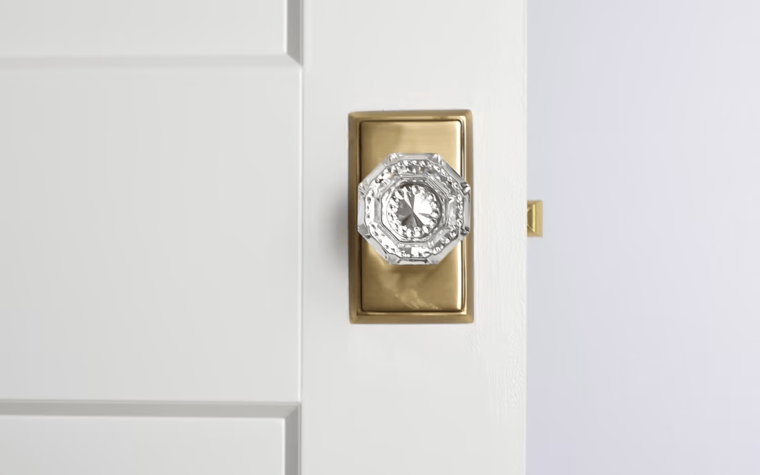 Close-up of an octagonal glass door knob attached to a brass plate on a white door.