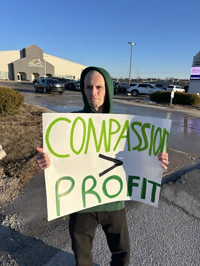 Craig holding a sign that reads that compassion is greater than profit.jpg