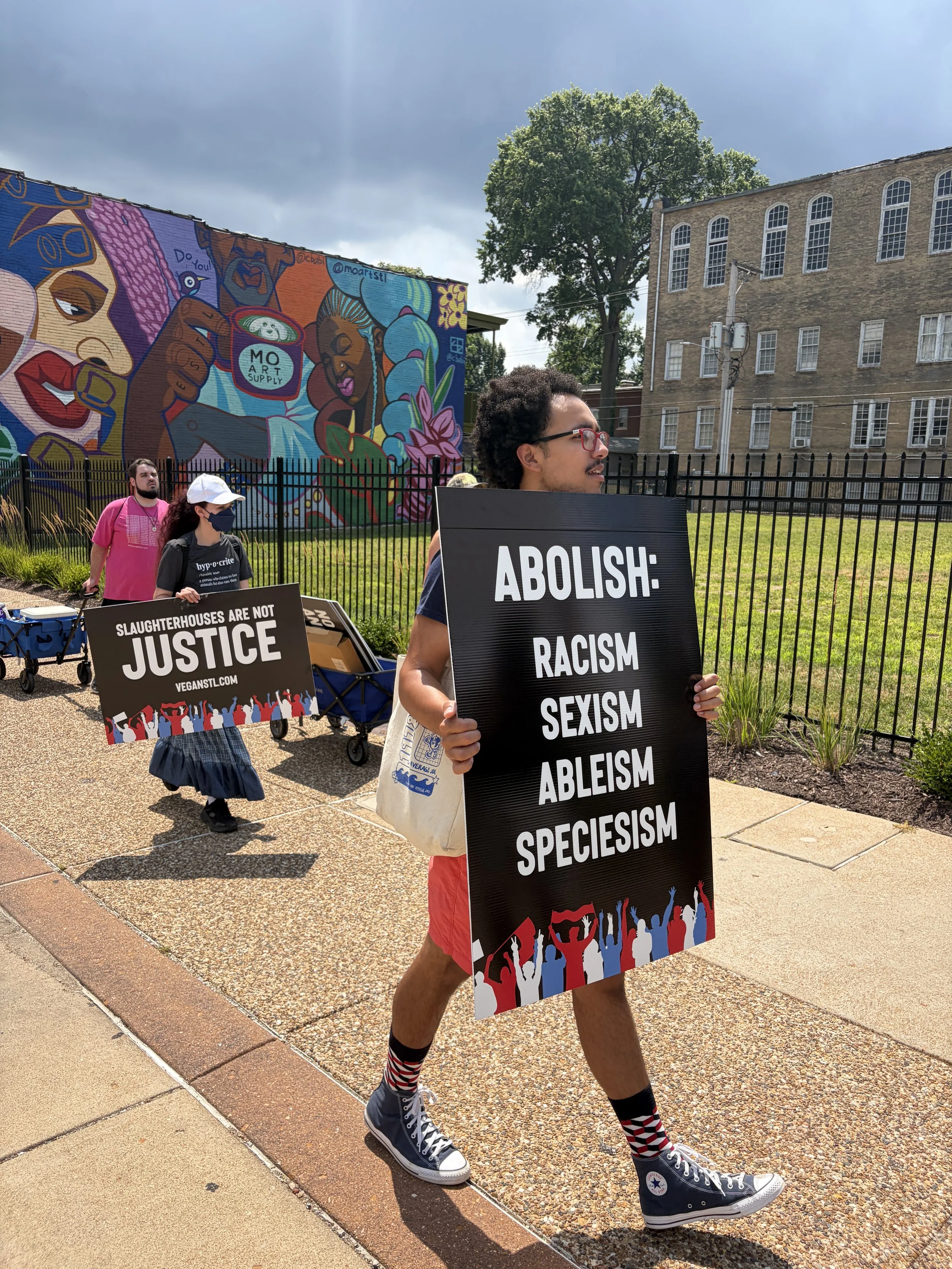 Julian carrying a sign that demands we abolish racism, sexism, ableism, and speciesism