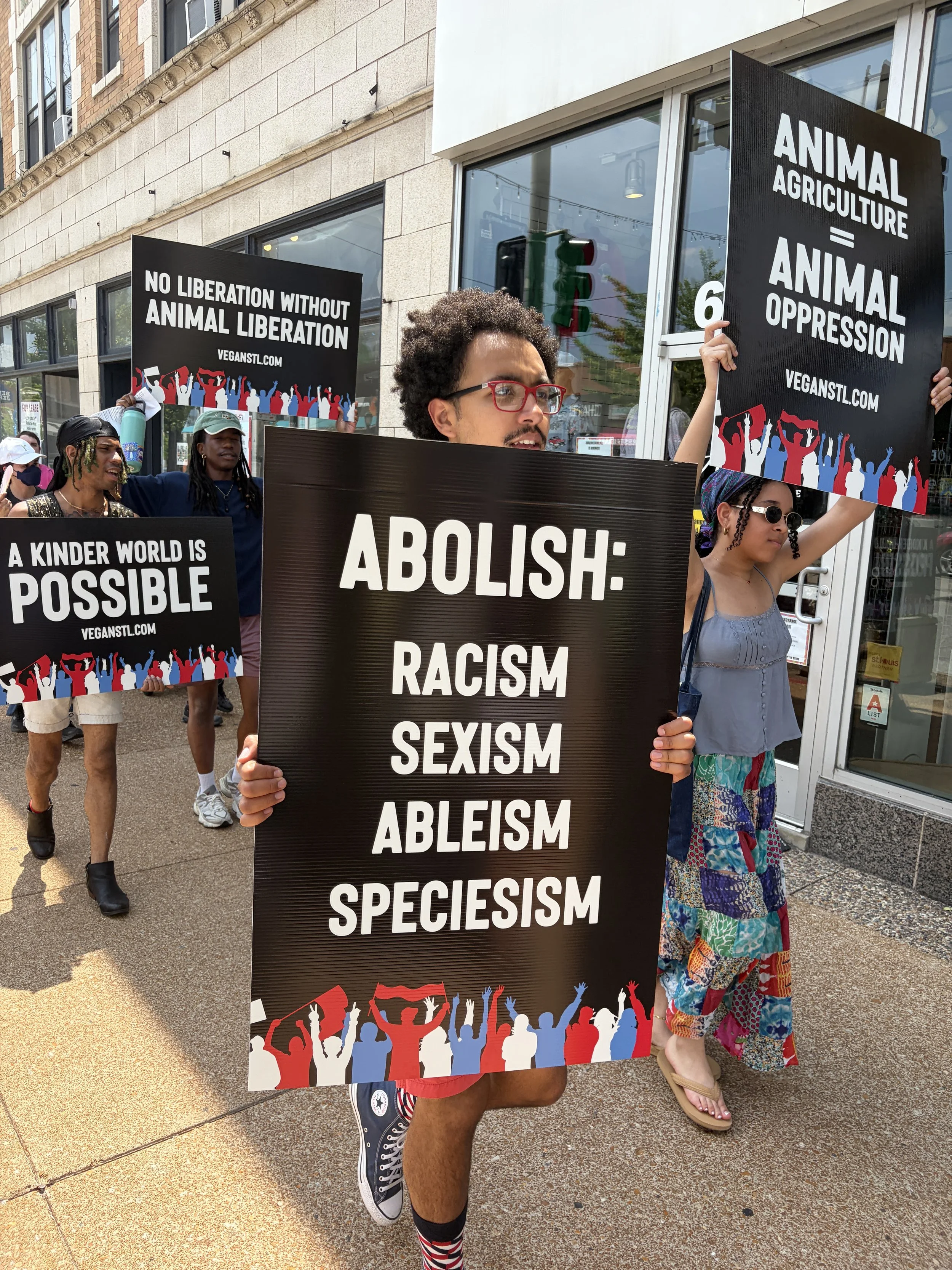 Julian marching with a sign that demands we abolish racism, sexism, ableism, and speciesism