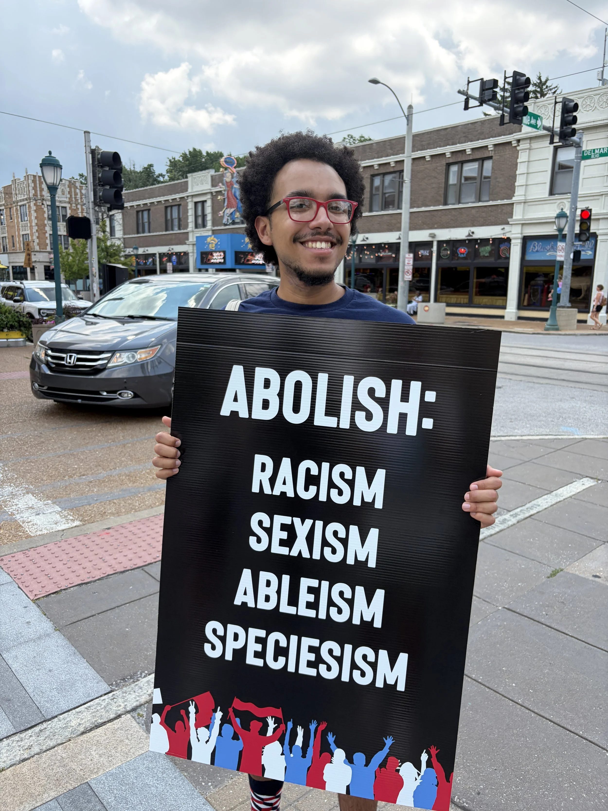 Julian proudly displaying his sign, demanding we abolish racism, sexism, ableism, and speciesism