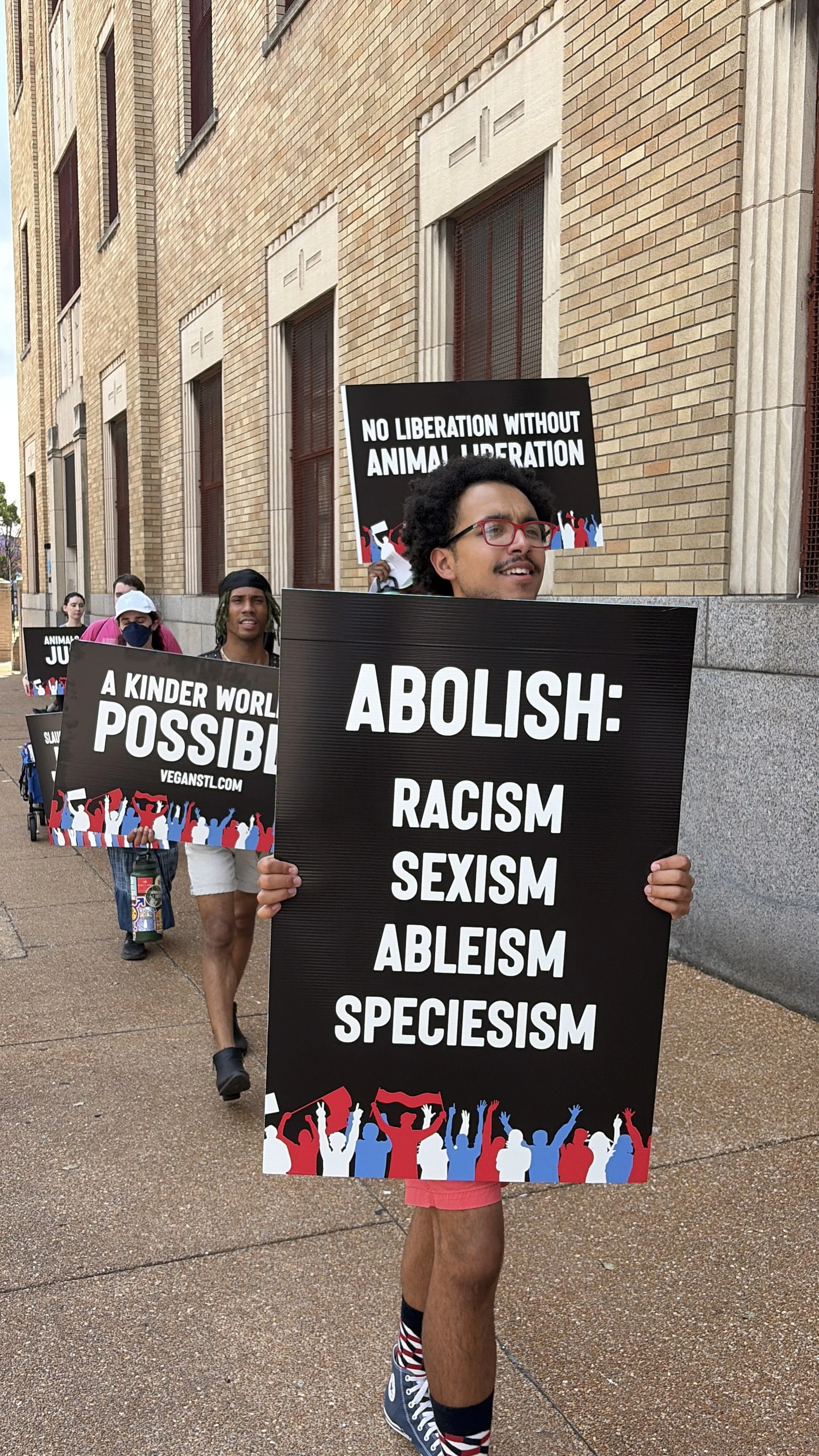 Julian, a vegan activist, carrying a sign demanding that we abolish oppression at our Animal Freedom March