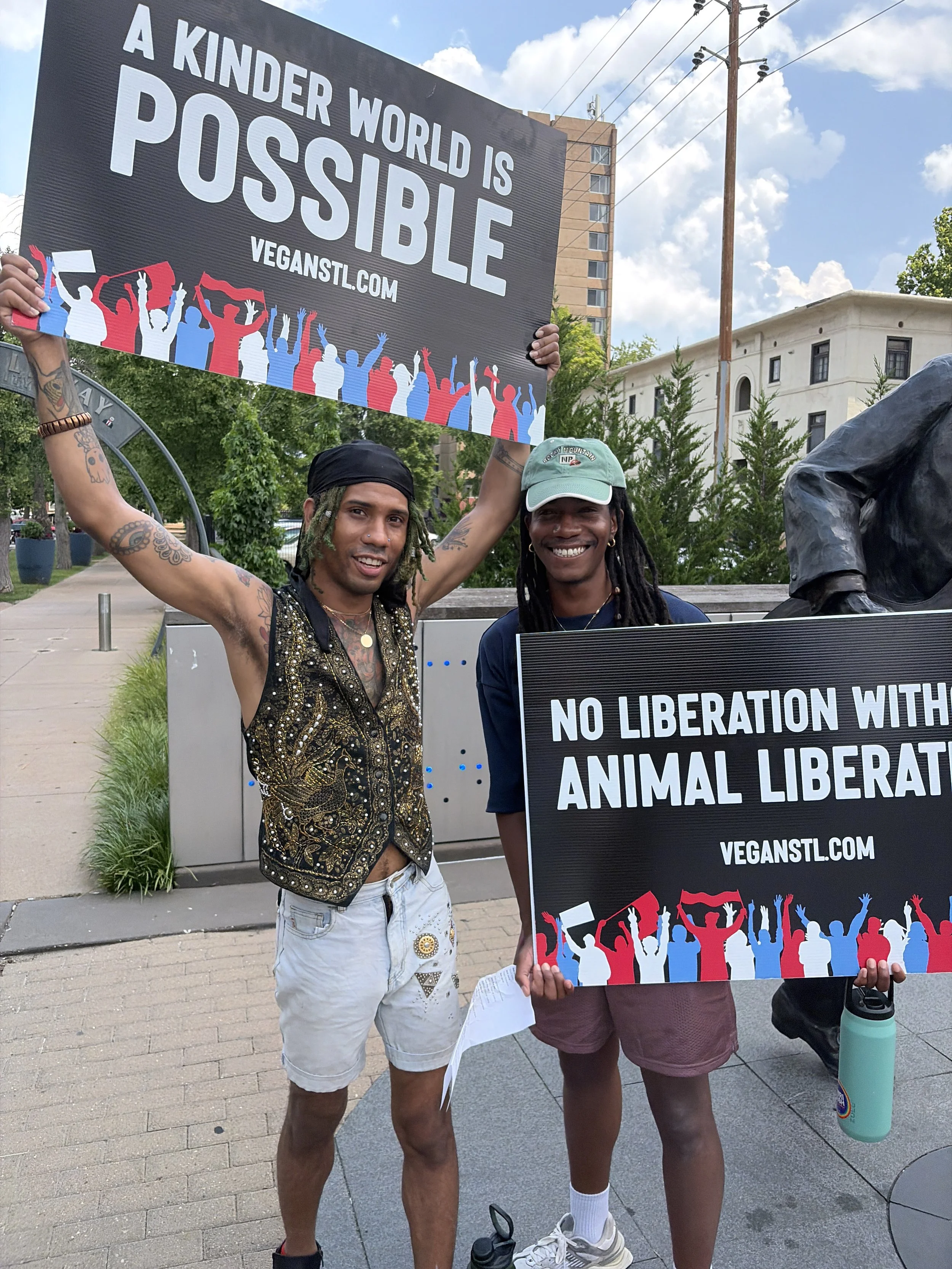 Maxi Glamour and their friend holding signs that read a kinder world is possible and no liberation without animal liberation