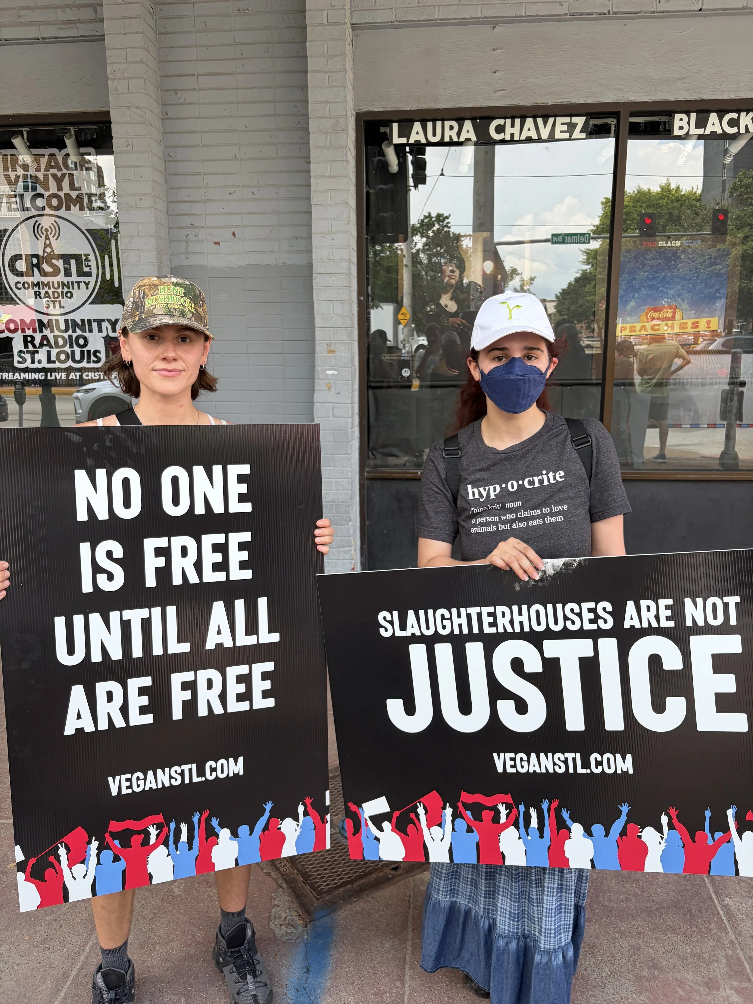 Two activists holding signs that read no one is free until all are free and slaughterhouses are not justice