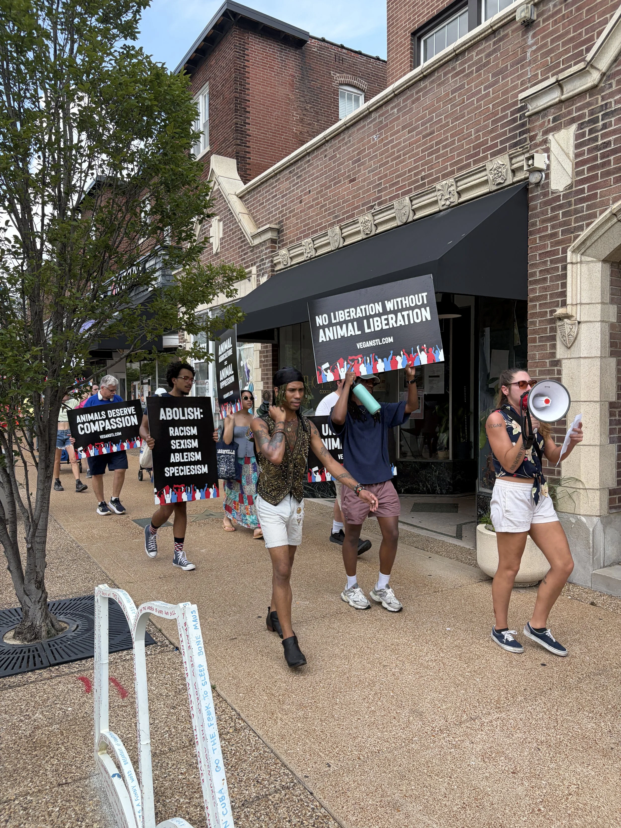 Vegan animal rights activists marching in front of storefronts along the Delmar Loop