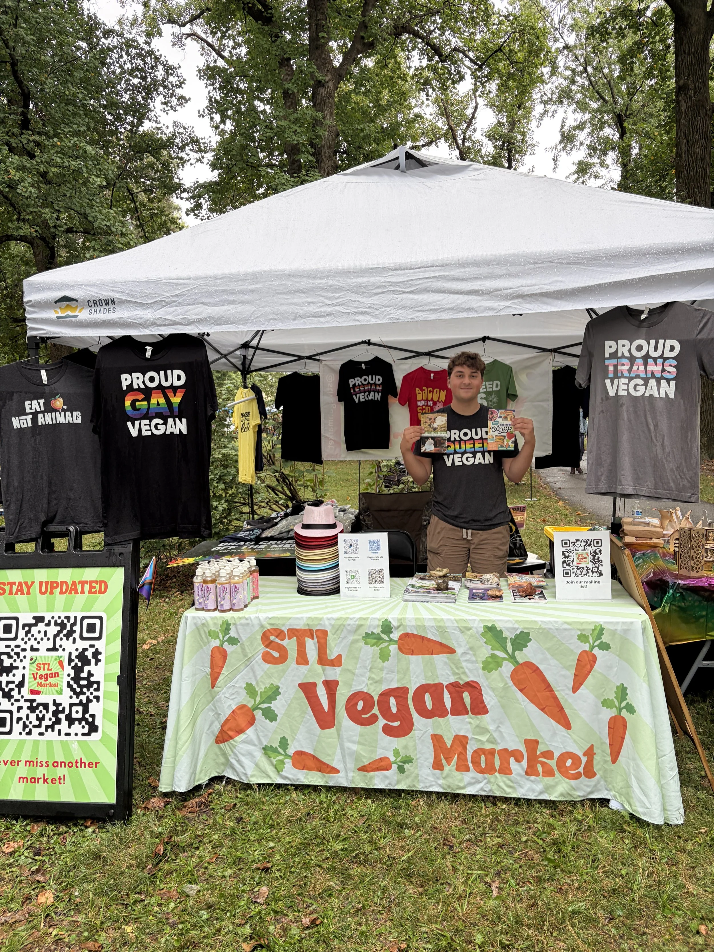 Troy at booth holding literature for Vegan Pride Booth at Tower Grove Pride in St. Louis, Missouri.png