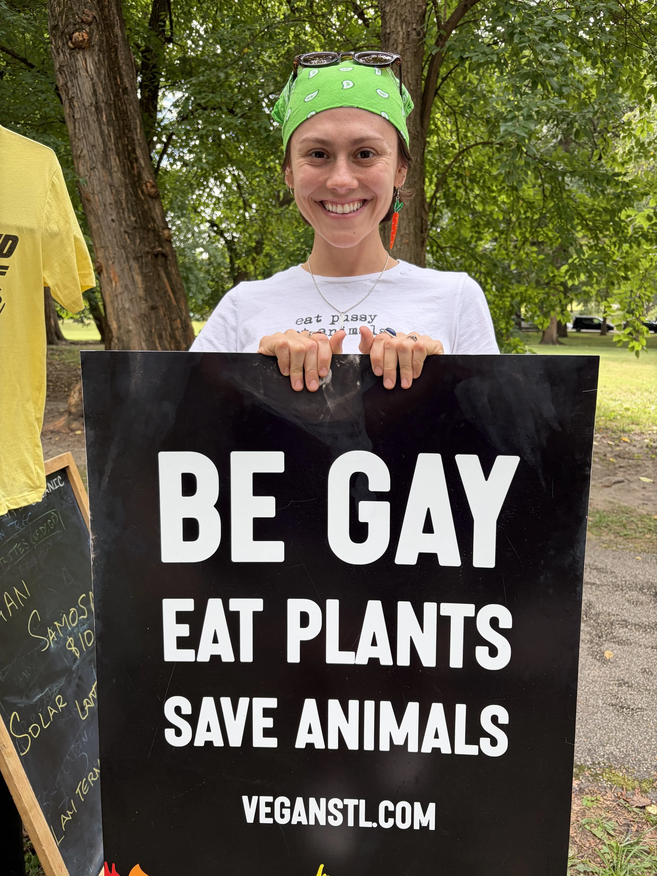 Jade holds Be Gay Eat Plants sign for Vegan Pride Booth at Tower Grove Pride in St. Louis, Missouri.png