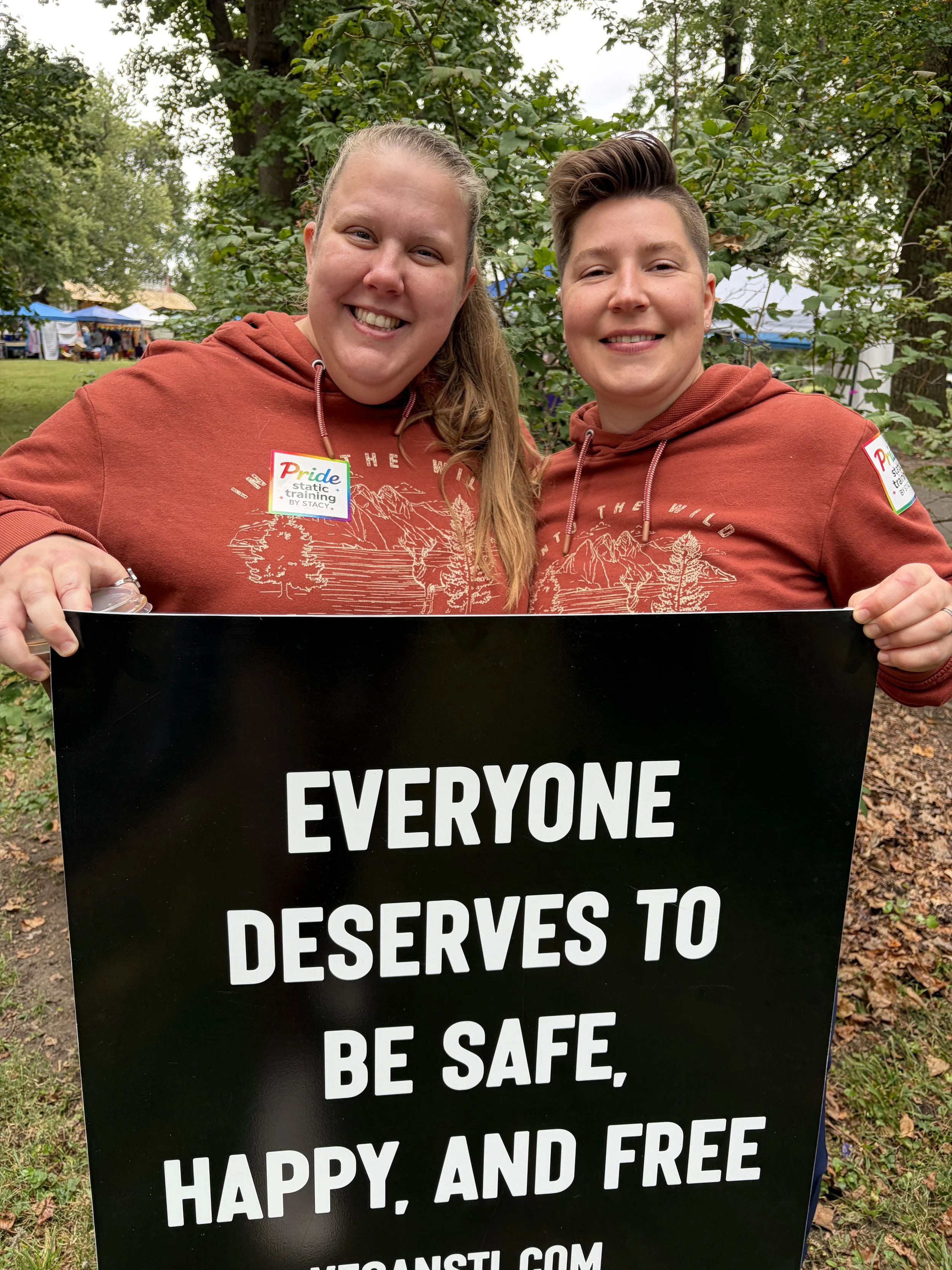 Booth visitors hold sign at Vegan Pride Booth at Tower Grove Pride in St. Louis, Missouri.png