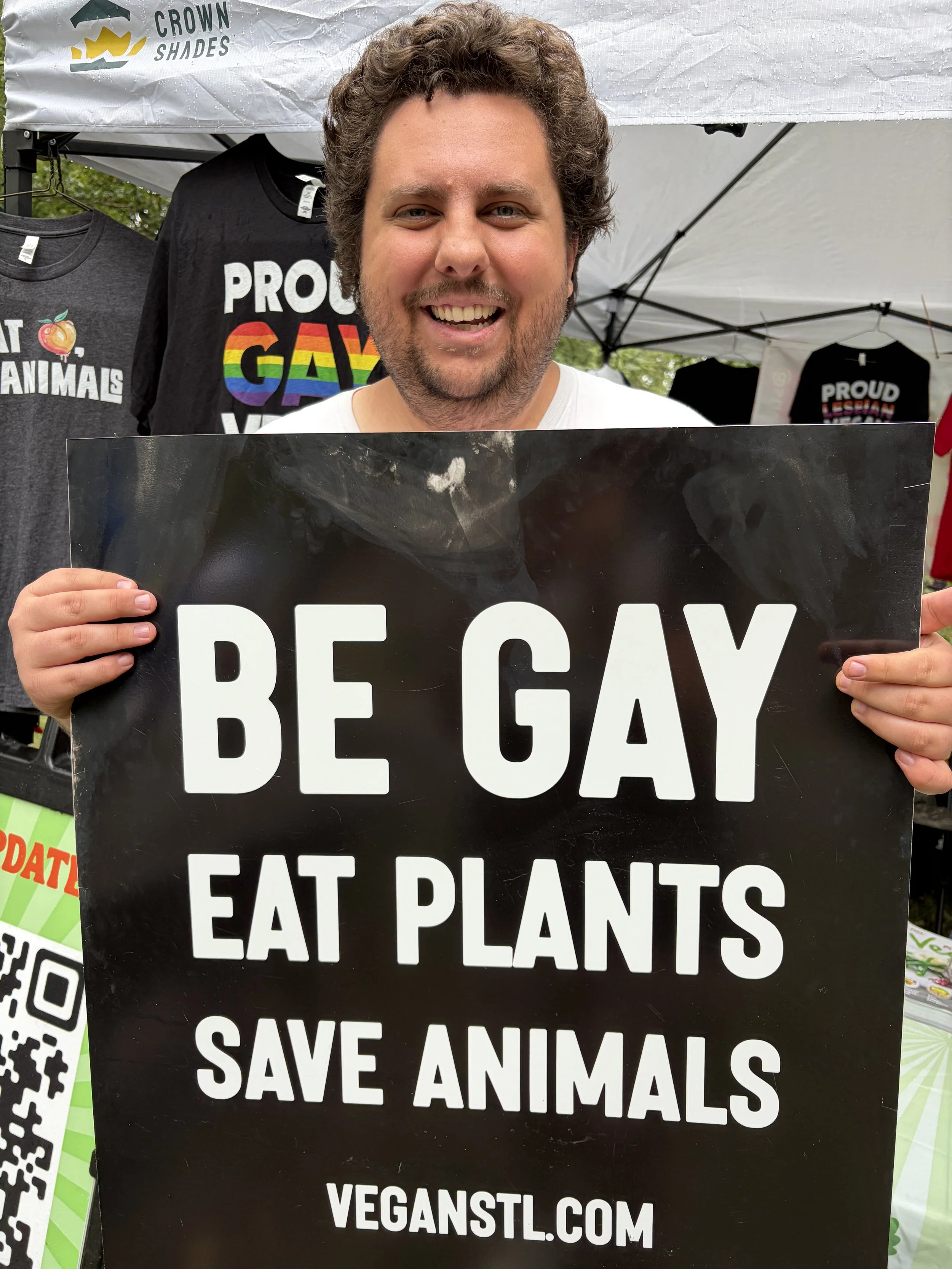 Kyle holds Be Gay Eat Plants sign at Vegan Pride Booth at Tower Grove Pride in St. Louis, Missouri.png