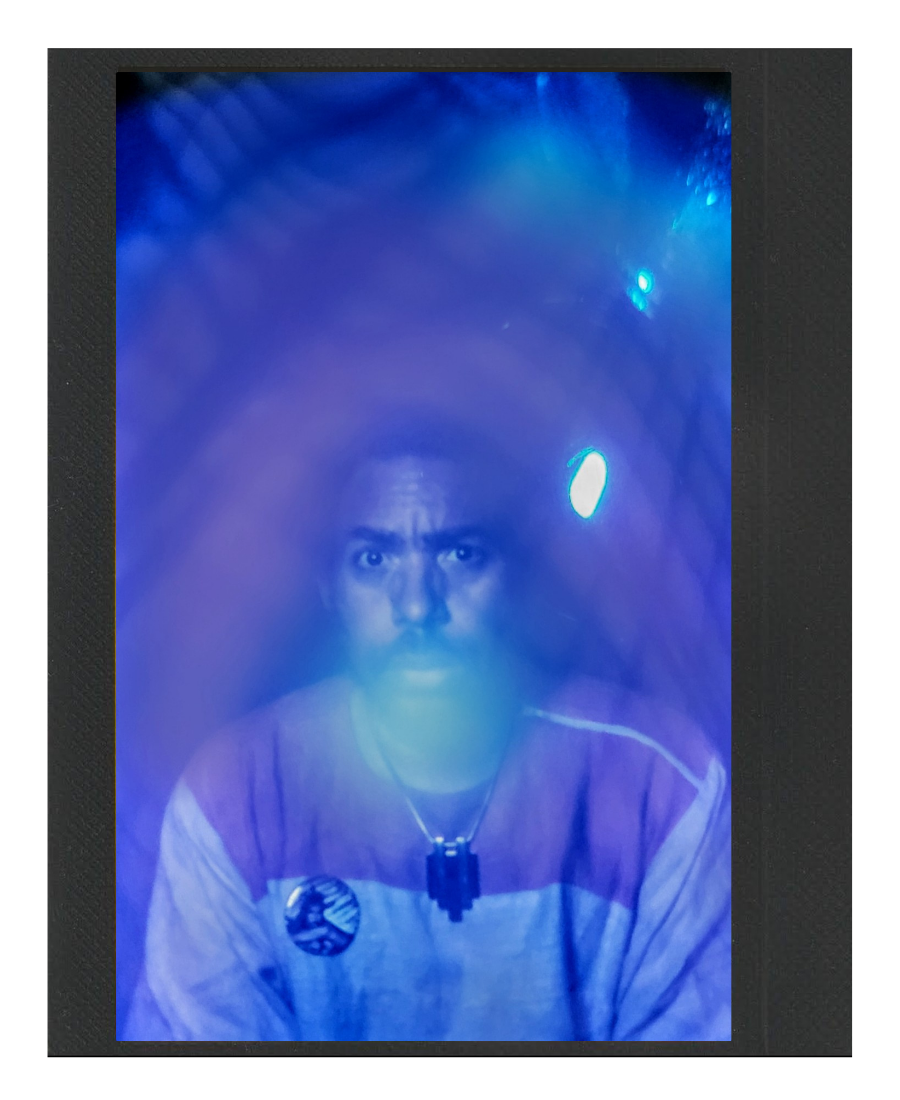 A young man with a surprised expression, face illuminated by blue lights, looking into a transparent surface with reflections and a black border.
